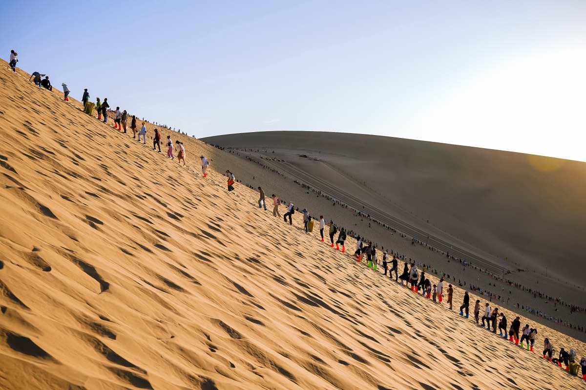 Persone in salita sulle dune di Mingsha a Dunhuang