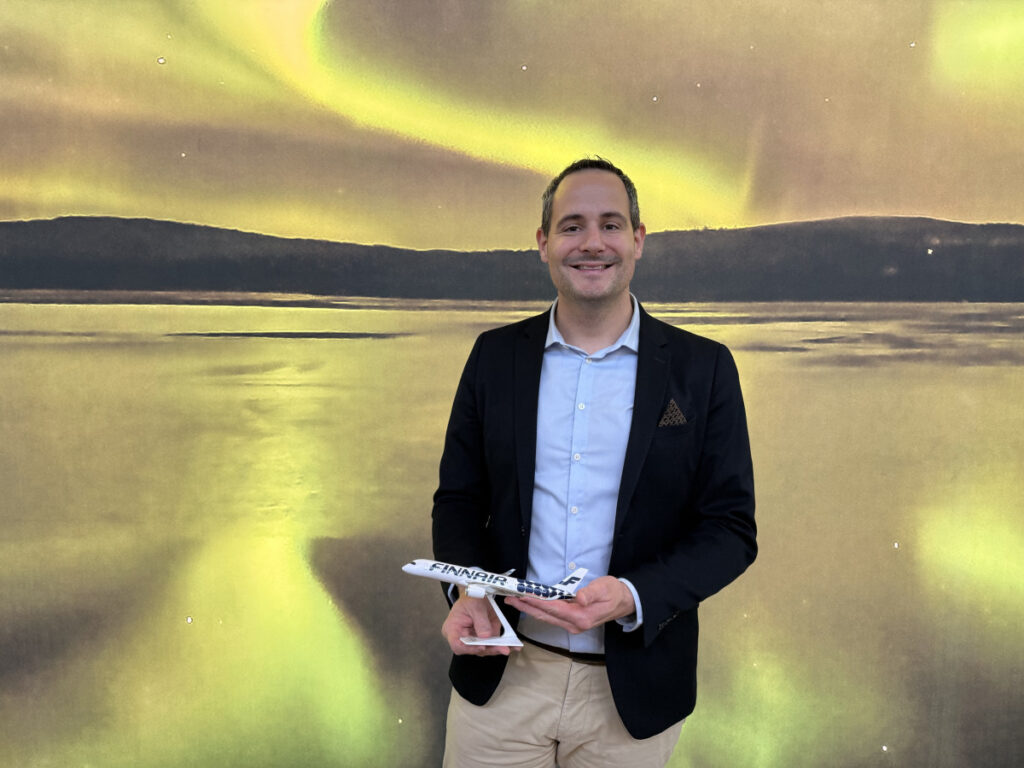 Geoffrey Carrage di Finnair con un modellino di aereo Finnair allo stand del TTG Travel Experience 2026